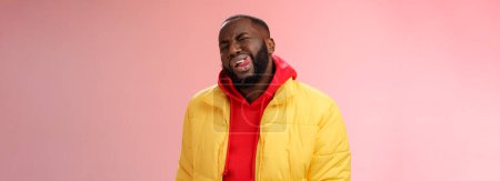 Téléchargez les photos : Cheeky élégant drôle homme barbu africain en veste jaune à la mode sweat à capuche rouge montrer la langue sassy flirt regard clin d'oeil caméra essayer d'impressionner femme feindre macho, debout fond rose. - en image libre de droit
