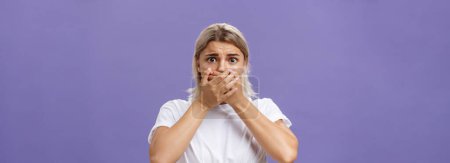 Photo for Waist-up shot of shocked nervous and scared young woman witnessing terrible crime covering mouth with both hands not to scream frowning staring frightened at camera over purple background. Emotions - Royalty Free Image