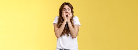 Photo for Shocked speechless scared stunned curly-haired caucasian woman gasping hold fingers mouth biting nails stare camera frightened express fear terrified scary movie stand yellow background. - Royalty Free Image