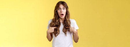 Photo for Shocked concerned questioned curly-haired girl drop jaw gasping stare offended surprised pointing herself feel accused reacting blame shook misunderstanding stand yellow background insulted. - Royalty Free Image