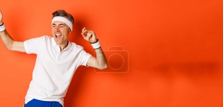 Téléchargez les photos : Portrait d'un homme d'âge moyen en bonne santé et actif, faisant du sport et se sentant bien, dansant sur fond orange en vêtements de sport. - en image libre de droit