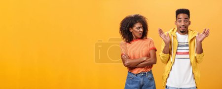 Photo for Jeez man what your problem. Offended displeased african american stylish and attractive girlfriend looking at boyfriend acting cool pretending he uninvolved shrugging with sorry look and smiling - Royalty Free Image