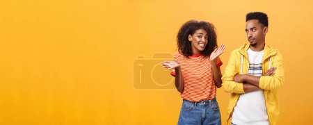 Photo for Guy thinks his friend weirdo making dumb thinks looking at cute girl with suspicious look crossing arms on chest raising eyebrow questioned while girlfriend saying sorry shrugging over orange wall - Royalty Free Image