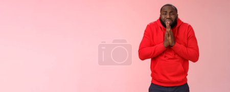 Photo for Miserable african american man beard in red hoodie stooping make supplicating upset grimace grying sobbing asking help say please hold hands pray begging mercy, apologizing need money. - Royalty Free Image