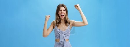 Photo for Excited and thrilled overwhelmed attractive woman in matching stylish clothes becoming fan of football standing on stadium yelling to cheer team raising clenched fists in rage and victory gesture - Royalty Free Image