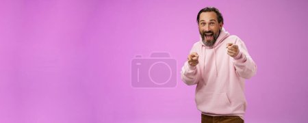 Photo for Gotcha. Portrait carefree funny amusing adult energized bearded man jumping pranking friend having fun laughing happily pointing camera index fingers greeting picking you, purple background. - Royalty Free Image