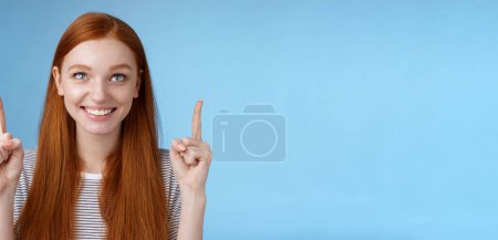 Photo for Cheerful curious amused happy entertained redhead pretty girl gazing pointing up smiling approval like interesting product watching perfomance enjoy cool holiday promos, standing blue background. - Royalty Free Image