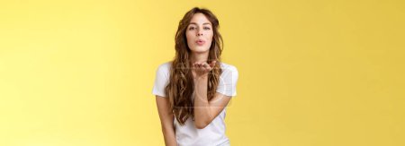 Photo for Tender lovely charming sensual curly-haired glamour female sending you passionate flirty kiss blow muah camera gazing hold palm near folded lips romantic sympathy attitude stand yellow background - Royalty Free Image