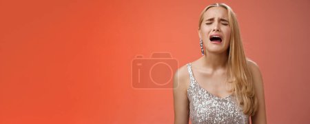 Photo for Immature whining spoiled adult rich daughter blond long hair in silver stylish dress complaining sad cruel unfair life crying sobbing frowning sulking upset, standing disappointed red background. - Royalty Free Image