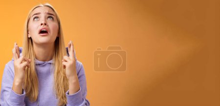 Photo for Worried nervous cute blond woman in hoodie begging god help cross fingers good luck supplicating look up skies wanna win anticipating good news anxiously awaiting, orange background. - Royalty Free Image