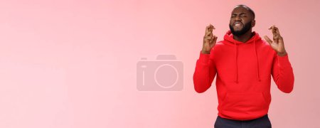 Photo for Passionate devoted african-american male fan praying cross fingers good luck asking god win bet biting lip impatiently waiting important results supplicating hopefully, standing pink background. - Royalty Free Image
