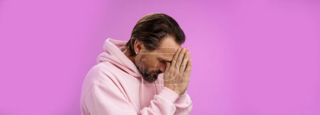 Photo for Concerned upset man supplicating asking god mercy help praying bow head close eyes hold hands pray hopefully waiting miracle worried wife health, standing sadness purple background. Copy space - Royalty Free Image