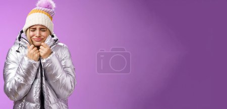 Photo for Unhappy sobbing whining cute blond girl pull jacket tight body close eyes crying freezing cold standing snowy winter resort shaking low temparature, purple background suffering discomfort. - Royalty Free Image