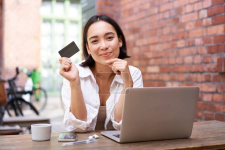 Photo for Stylish young asian woman doing shopping online, sitting with credit card and laptop, buying in internet and paying contactless, dealing with bills. - Royalty Free Image