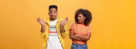 Photo for Jeez man what your problem. Offended displeased african american stylish and attractive girlfriend looking at boyfriend acting cool pretending he uninvolved shrugging with sorry look and smiling - Royalty Free Image