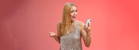 Photo for Troubled concerned arrogant young blond woman complaining yelling smartphone cannot call friend no signal holding smartphone look mobile display pissed moody arguging, red background. - Royalty Free Image