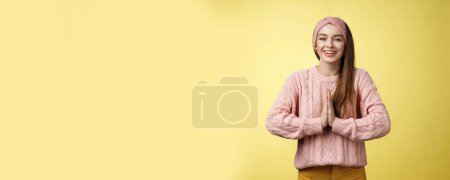 Photo for Please do me favour. Charming young female student wearing knitted sweater, headband pressing palms together in pray begging, asking for help smiling thankful, grateful for effort over yellow wall. - Royalty Free Image
