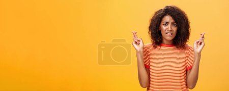 Photo for Waist-up shot of concerned troubled nervous african american woman with curly hairstyle biting lower lip anxiously frowning crossing fingers for good luck hopefully praying for dream come true - Royalty Free Image