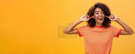 Photo for Do not care what saying cannot hear you. Carefree indifferent good-looking african american woman with curly hairstyle closing ears with index finger singing lalala during argument behaving childish. - Royalty Free Image