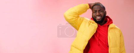Photo for Upset gloomy african-american bearded guy in yellow jacket red hoodie hold hands cringing regret face disaster terrible situation expressing sorrow crying sobbing, standing pink background. - Royalty Free Image