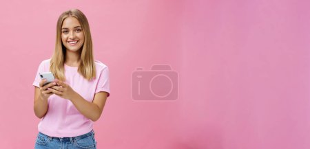 Téléchargez les photos : Femme appelant taxy via smartphone demandant l'adresse d'un ami souriant joyeusement à la caméra tenant le téléphone avec les deux mains sur la poitrine entrer en contact avec les clients via des messages debout sur le mur rose - en image libre de droit
