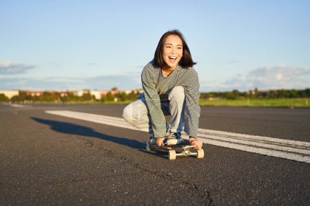 Téléchargez les photos : Portrait de sans soucis, heureux asiatique fille patinage, équitation planche à roulettes et rire, profiter de la journée ensoleillée. - en image libre de droit