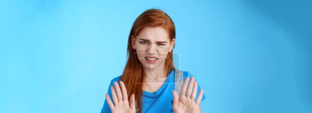 Photo for Close-up uninterested displeased ignorant picky redhead girlfriend, frowning make disgusted grimace raise hands block stop gesture, refuse, waving arms no rejection sign, stand blue background. - Royalty Free Image
