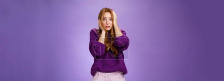 Photo for Girl in stupor feeling shocked and troubled as realising huge mistake made, holding hands on face and head popping eyes at camera confused and hopeless, posing anxious over purple background. - Royalty Free Image