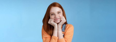 Photo for Tenderness, wellbeing, beauty conept. Attractive young ginger girl pure skin blue eyes lean palms silly smiling camera look amused enthusiastic listen interesting stories gladly, blue background. - Royalty Free Image