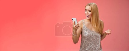 Photo for Troubled concerned arrogant young blond woman complaining yelling smartphone cannot call friend no signal holding smartphone look mobile display pissed moody arguging, red background. - Royalty Free Image