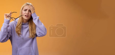 Photo for Upset gloomy bothered blond girl take-off glasses cringing grimacing feel unwell suffering headache standing dizzy touching forehead painful migraine bothering working woman, orange background. - Royalty Free Image