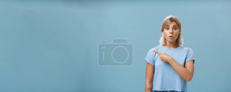 Photo for Studio shot of amazed stunned cute blonde witnessing unbelievable event gasping opening mouth staring astonished and pointing left being questioned and shocked over blue background. Emotions concept - Royalty Free Image