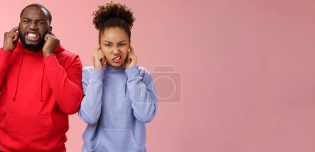 Photo for Irritated annoyed couple african american siglings man woman cringing discomfort close ears plug fingers unhear terrible disgusting noise standing bothered grimacing hear awful sound. - Royalty Free Image