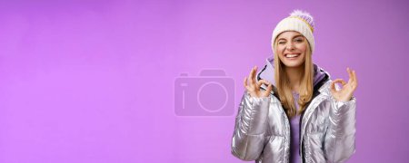 Photo for Sassy attractive blond girl in outdoor stylish jacket hat hoodie show no problem okay perfection gesture satisfied good hotel quality smiling broadly winking cheeky camera, enjoying holidays. - Royalty Free Image