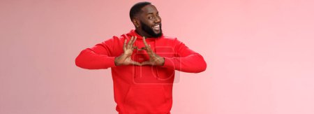 Photo for Someone love ya. Portrait enthusiastic creative cute black boyfriend wearing red hoodie show heart sign smiling broadly confessing love sympathy look passionate, express romance pink background. - Royalty Free Image