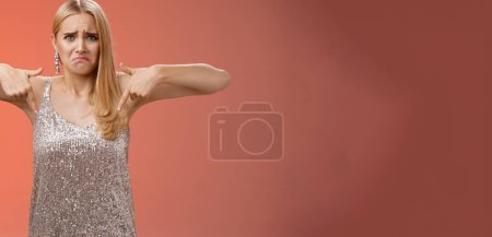 Photo for Whining complaining upset depressed blond woman in silver dress crying boyfriend broke-up prom night standing unhappy expressing sorrow regret disappointment pointing down red background. - Royalty Free Image
