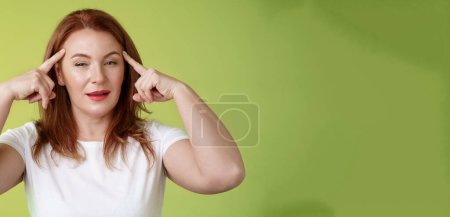 Photo for Smart choice. Intrigued thoughtful good-looking assertive redhead creative middle-aged woman touch temples squinting pondering info thinking use mental power read minds stand green background. - Royalty Free Image