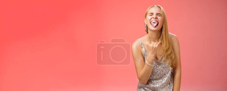 Photo for Lifestyle. Excited carefree entertained blond in silver glittering evening dress partying having fun amused show tongue close eyes rock-n-roll gesture heavy metal enjoying awesome celebration - Royalty Free Image