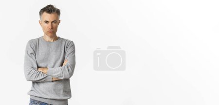 Photo for Image of angry middle-aged man feeling offended, cross arms on chest and squinting at camera, standing over white background. - Royalty Free Image