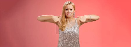 Photo for Whining complaining upset depressed blond woman in silver dress crying boyfriend broke-up prom night standing unhappy expressing sorrow regret disappointment pointing down red background. - Royalty Free Image