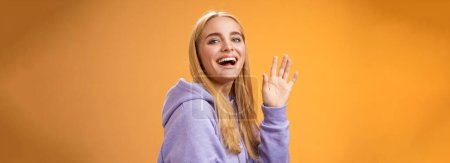 Photo for Waist-up friendly lucky cute blond girl waving palm happily smiling turning camera greet friend say hello hi see familiar person welcoming newcomers joyfully, standing orange background. - Royalty Free Image