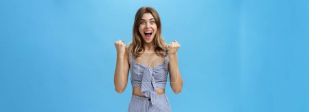Photo for Happy surprised and triumphing young nice girl with wavy natural hairstyle in matching striped outfit raising clenched fists in cheer and joy celebrating success or fortune smiling broadly at camera - Royalty Free Image