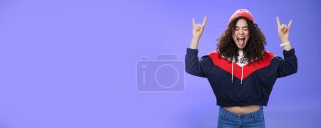 Photo for Waist-up shot of rebellious and carefree woman having fun feeling excited and awesome at party close eyes sticking out tongue and showing rock-n-roll signs, wearing beanie and warm clothes. - Royalty Free Image