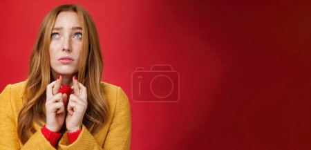 Photo for Close-up shot of sad and nervous hopeful upset redhead female looking up faithfully, frowning concerned crossing fingers as praying and supplicating worried over red background. Emotions and body - Royalty Free Image