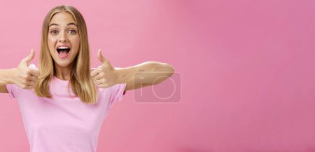 Téléchargez les photos : Petite amie de soutien acclamant pour le joueur préféré montrant pouces vers le haut avec sourire positif heureux donnant l'approbation et montrant qu'elle aime idée parfaite posant amusé et enthousiaste sur fond rose - en image libre de droit
