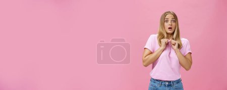 Photo for Woman gasping from fright being scared by someone pressing clenched hands to chest bending backwards looking worried and terrified at camera being shocked with unexpected bang over pink wall. Copy - Royalty Free Image