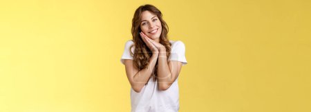 Photo for Tender feminine cute lovely woman curly hairstyle tilt head lay face palms delighted smiling broadly look admiration joy sympathy stand yellow background relaxed, sighing happily resting. - Royalty Free Image