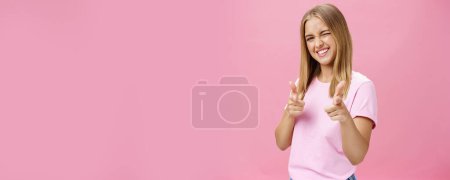 Téléchargez les photos : Femme exprimant une attitude positive envers la caméra pointant avec les doigts et clignant des yeux souriant joyeusement être soulevé, debout de bonne humeur avec des gestes optimistes sur fond rose. Espace de copie - en image libre de droit