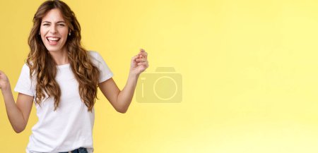 Téléchargez les photos : Sassy insouciant joyeux attrayant femme ayant plaisir à faire la fête écouter cool nouvelle chanson artiste préféré danse lever la main vers le haut en louchant cheeky regarder caméra lèvre synchronisation tenir smartphone fond jaune - en image libre de droit