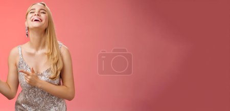 Photo for Funny carefree blond european woman in silver glittering evening dress raise head up close eyes laughing happily pointing left see hilarious person joking fool around, standing red background. - Royalty Free Image